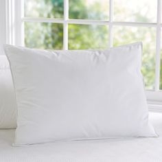 a white pillow sitting on top of a bed in front of a window next to pillows