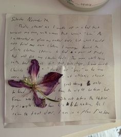 a piece of paper with writing on it and a flower laying on top of it