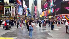 a crowd of people walking down a street next to tall buildings and billboards in times square