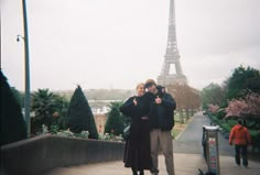 a man and woman standing next to each other in front of the eiffel tower