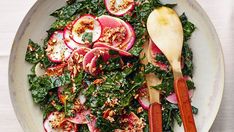 a white plate topped with greens and radishes next to two wooden spoons