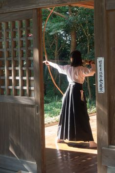 the woman is practicing her archery skills on the deck in front of an open door