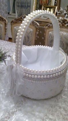 a white basket sitting on top of a table covered in pearls and ribbon, next to a mirror