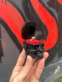 a hand holding a small skull ring with a red candle in it's mouth