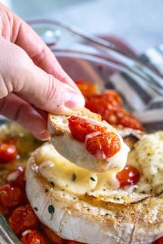 someone is dipping cheese on top of some food in a glass bowl with cherry tomatoes