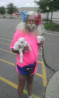 a man in pink shirt holding a white dog and drinking from a cup on street