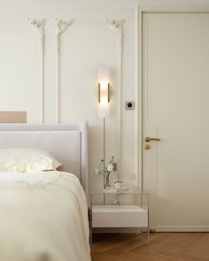 a white bed sitting in a bedroom next to a tall wall lamp on top of a wooden floor