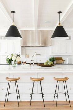 three stools in front of an island with two lights over it and flowers on the counter