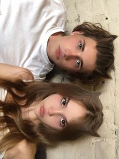 two young people laying on the ground with their heads close to each other and one has long brown hair