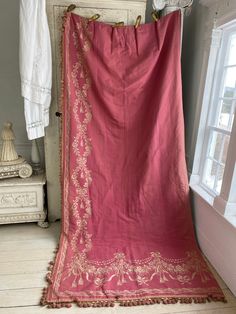 an old pink blanket is hanging on the wall next to a white dresser and window