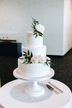 a three tiered white wedding cake on top of a round table with silverware