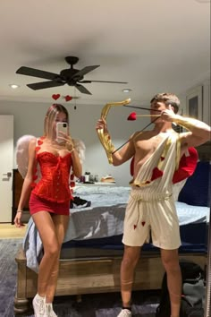 two people dressed up in costumes standing next to each other near a bed and ceiling fan