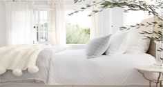 a bed with white linens and pillows in a bedroom next to a tree branch