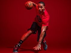 a man in red shirt and black shorts holding a basketball on his right hand while standing against a red background