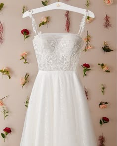 a wedding dress hanging on a hanger with flowers around it and the bride's bouquet