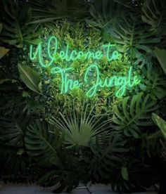 a neon sign that says welcome to the jungle in front of some green plants and leaves