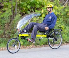 a man riding on the back of a yellow bike down a street next to lush green trees