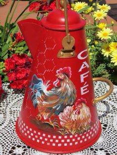 a red coffee pot with roosters painted on it and yellow flowers in the background