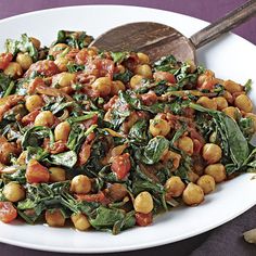 a white plate topped with spinach and chickpeas next to bread on a purple surface