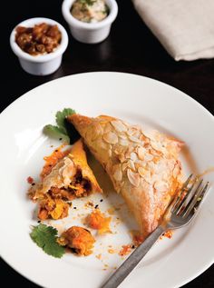 a white plate topped with a piece of pie next to a fork and bowl of nuts