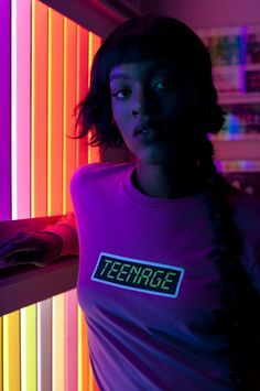 a woman standing in front of a neon colored wall with the word teenage on it