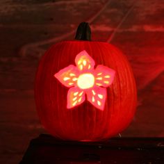 a lit up pumpkin with a flower on the front and side, sitting on a table