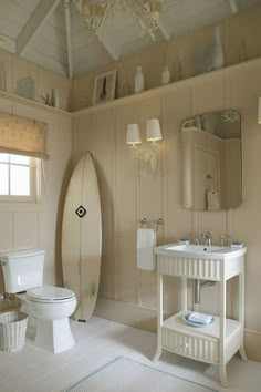 a white bathroom with a surfboard on the wall next to the toilet and sink