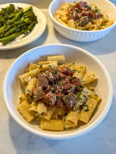 three white bowls filled with pasta and broccoli on top of a marble table