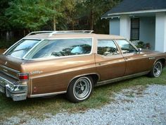 a brown station wagon parked in front of a house with trees and grass around it