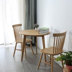 two wooden chairs and a table with books on it in front of a white wall