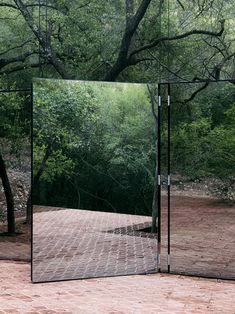 a large mirror sitting on top of a wooden floor in front of a green forest