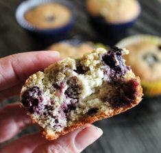 a hand holding a muffin with blueberries on it and other muffins in the background