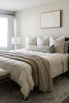 a bed with white linens and pillows in a bedroom next to a large window