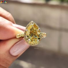 a yellow diamond ring is being held up by someone's hand in front of the camera