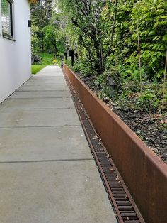 an empty sidewalk next to a building with trees in the back ground and bushes on either side