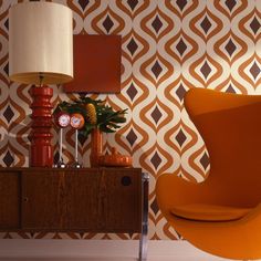 an orange chair sitting next to a lamp on top of a wooden table in front of a wall