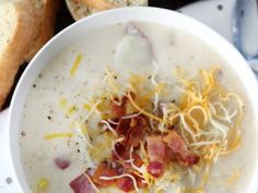 a bowl of soup with bacon and cheese in it next to some slices of bread