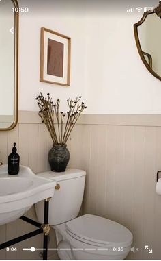 a white toilet sitting next to a sink in a bathroom under a mirror and framed pictures on the wall