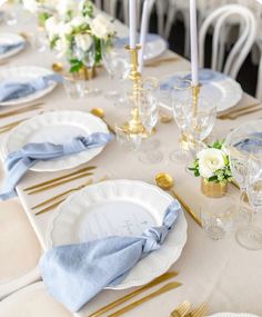 the table is set with gold and white plates, silverware, and blue napkins