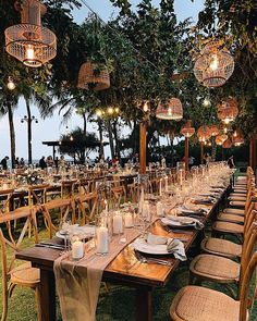 a long table set up with place settings and hanging lights for an outdoor wedding reception