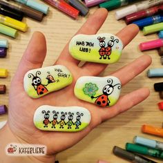 four painted rocks in the shape of ladybugs with words written on them and colored crayons around them