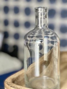 an empty glass bottle sitting on top of a wooden tray next to a blue and white tile wall