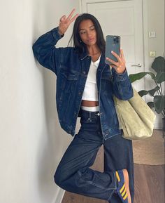 a woman taking a selfie with her cell phone while wearing jeans and adidas sneakers