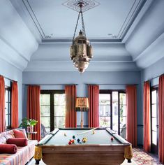 a pool table in the middle of a living room with red curtains and couches