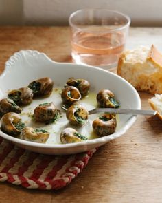 a white bowl filled with mushrooms next to bread and a glass of water on a wooden table