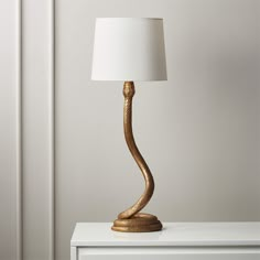 a gold lamp sitting on top of a white table next to a white dresser and wall