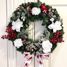 a christmas wreath with white flowers and red berries hanging on a front door, decorated with pine cones