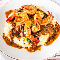 a white plate topped with shrimp and grits covered in gravy on top of mashed potatoes