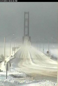 a snow covered road with traffic lights and street signs in the distance on a foggy day