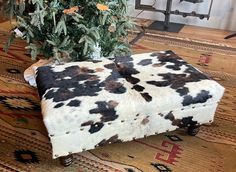 a cow print ottoman sitting on top of a rug next to a small christmas tree